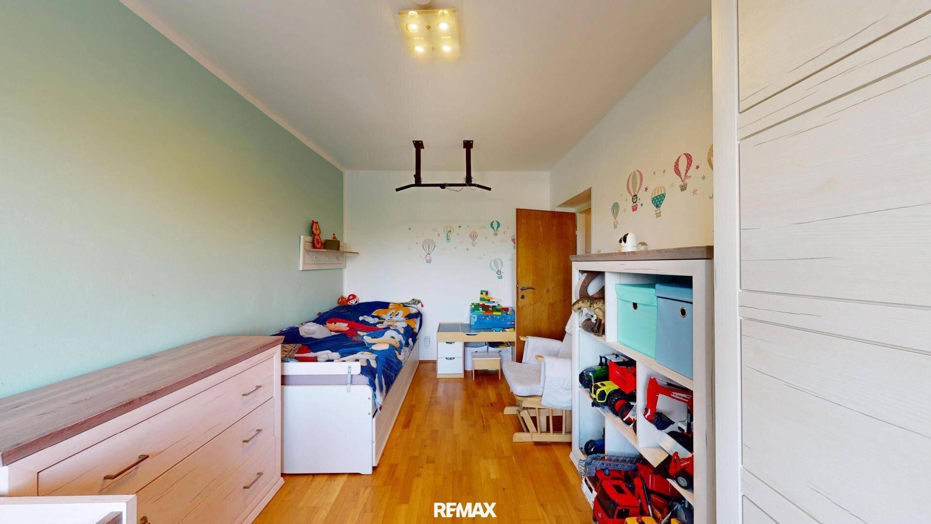 Freundliches Kinderzimmer mit Holzboden, Einzelbett und farbenfroher Wanddekoration.