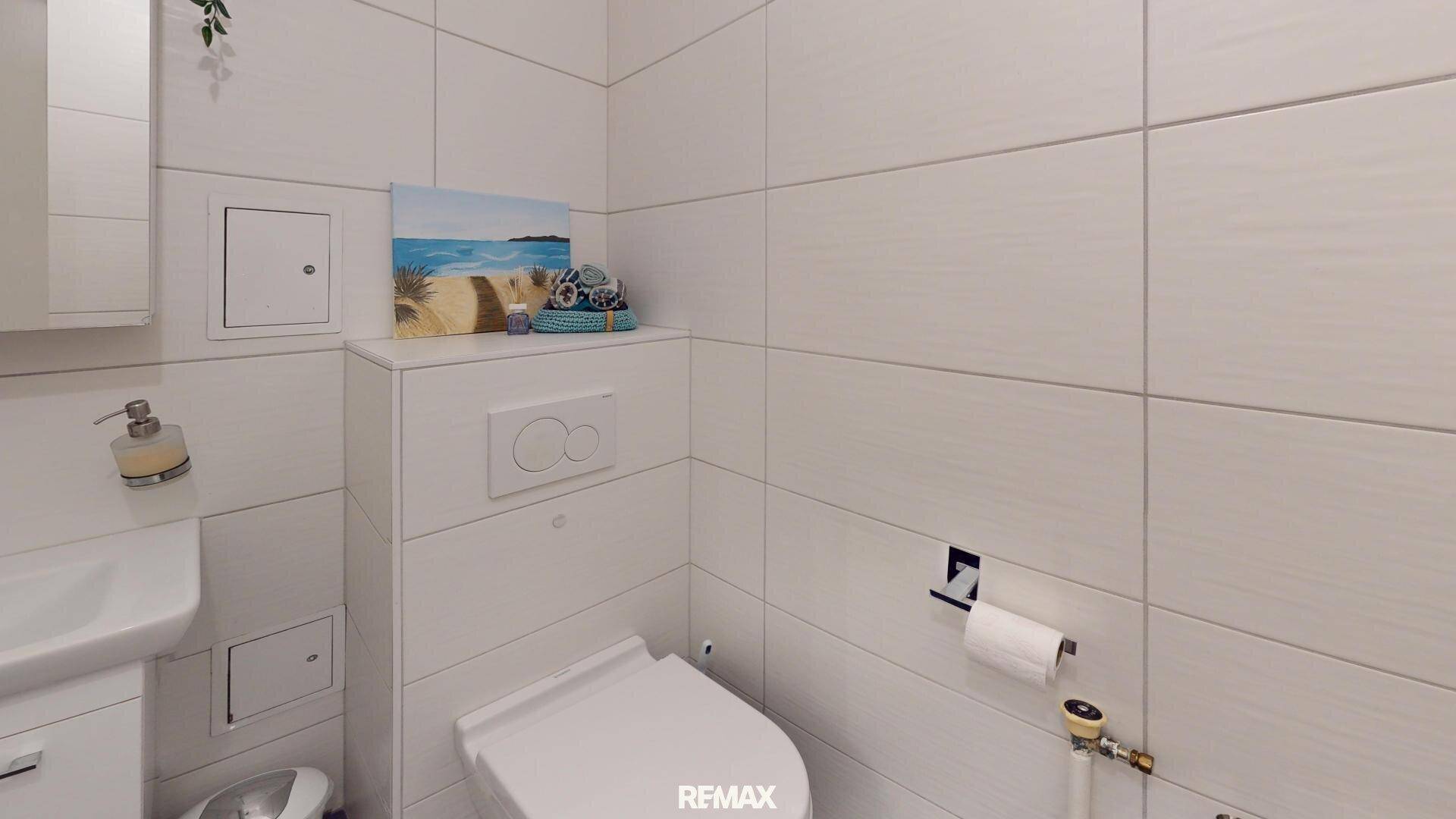 Modernes Gäste-WC mit wandhängender Toilette, kleinem Waschbecken und weißen Fliesen.