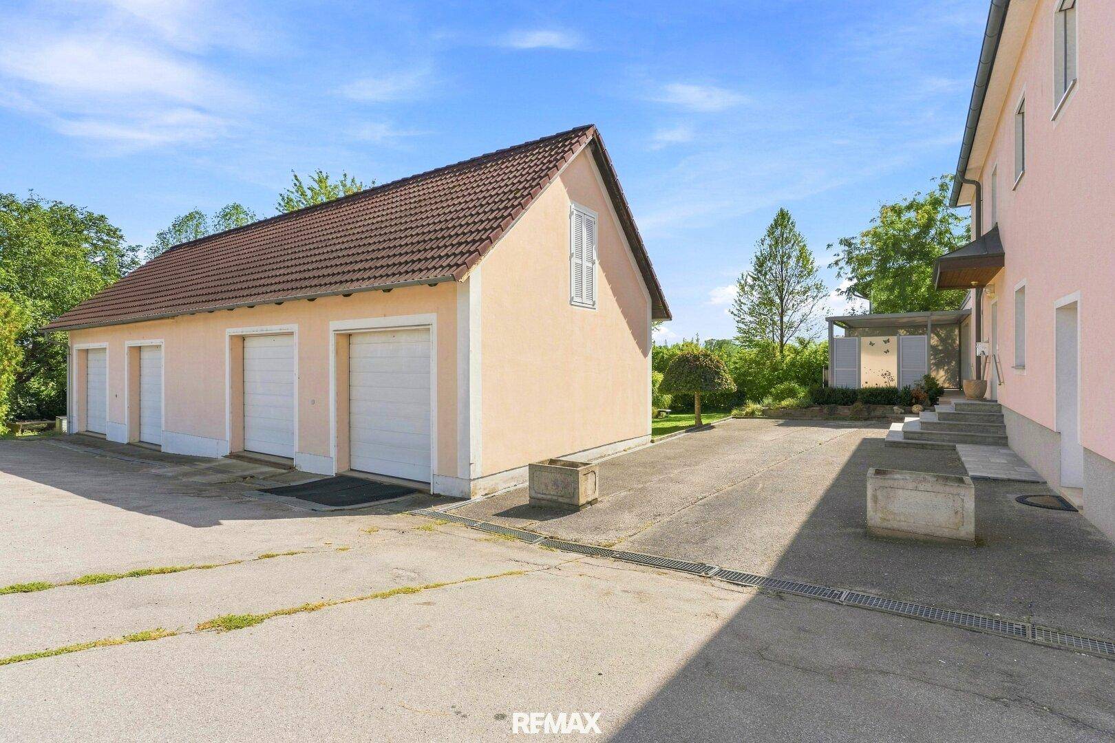 Separate Garage mit drei Toren und großzügiger gepflasterter Zufahrt zum Gebäude.