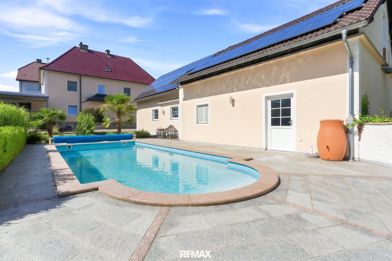 Außenbereich mit großem Swimmingpool, gepflasterter Terrasse und Solaranlage auf dem Dach.