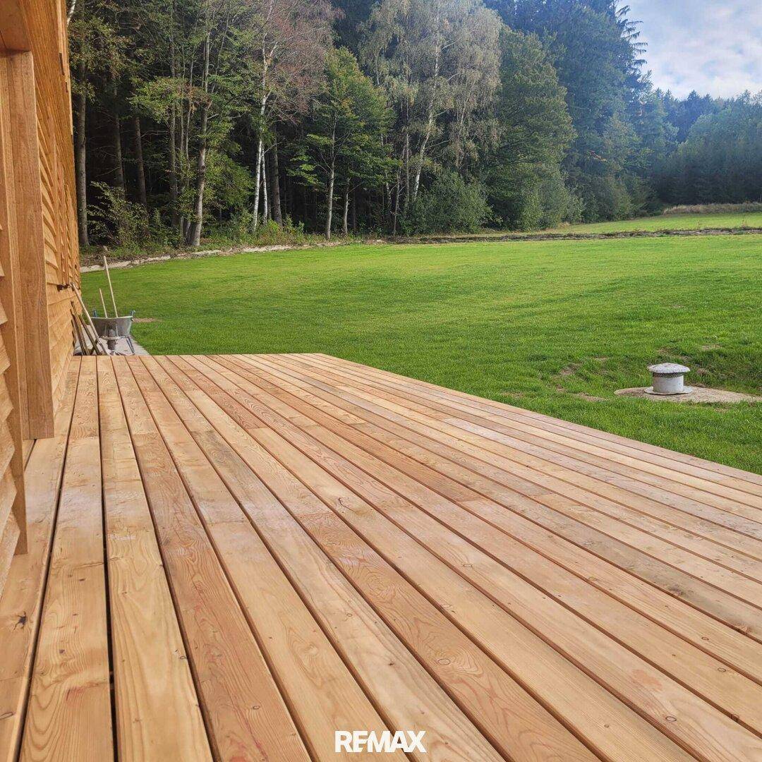 Geräumige Holzterrasse mit weitem Blick ins Grüne und angrenzendem Wald.