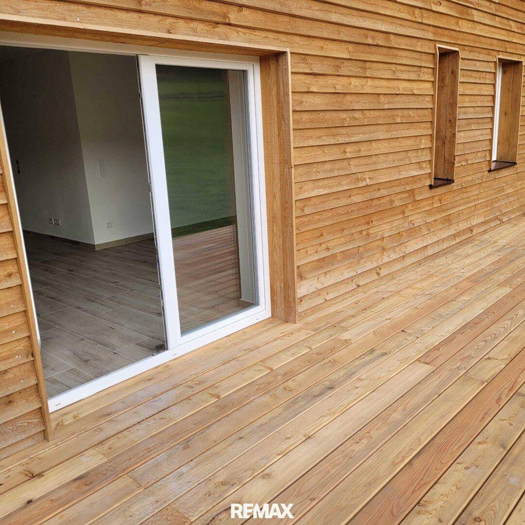 Holzterrasse mit Zugang zum Innenbereich durch eine große Glasschiebetür und Holzfassade.