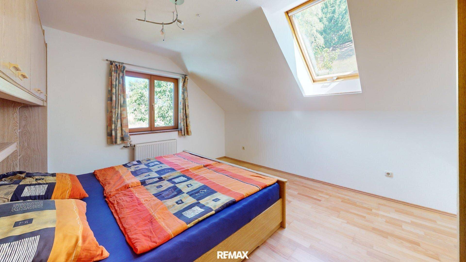 Gemütliches Schlafzimmer im Dachgeschoss mit Holzboden, Bett und Dachfenster.