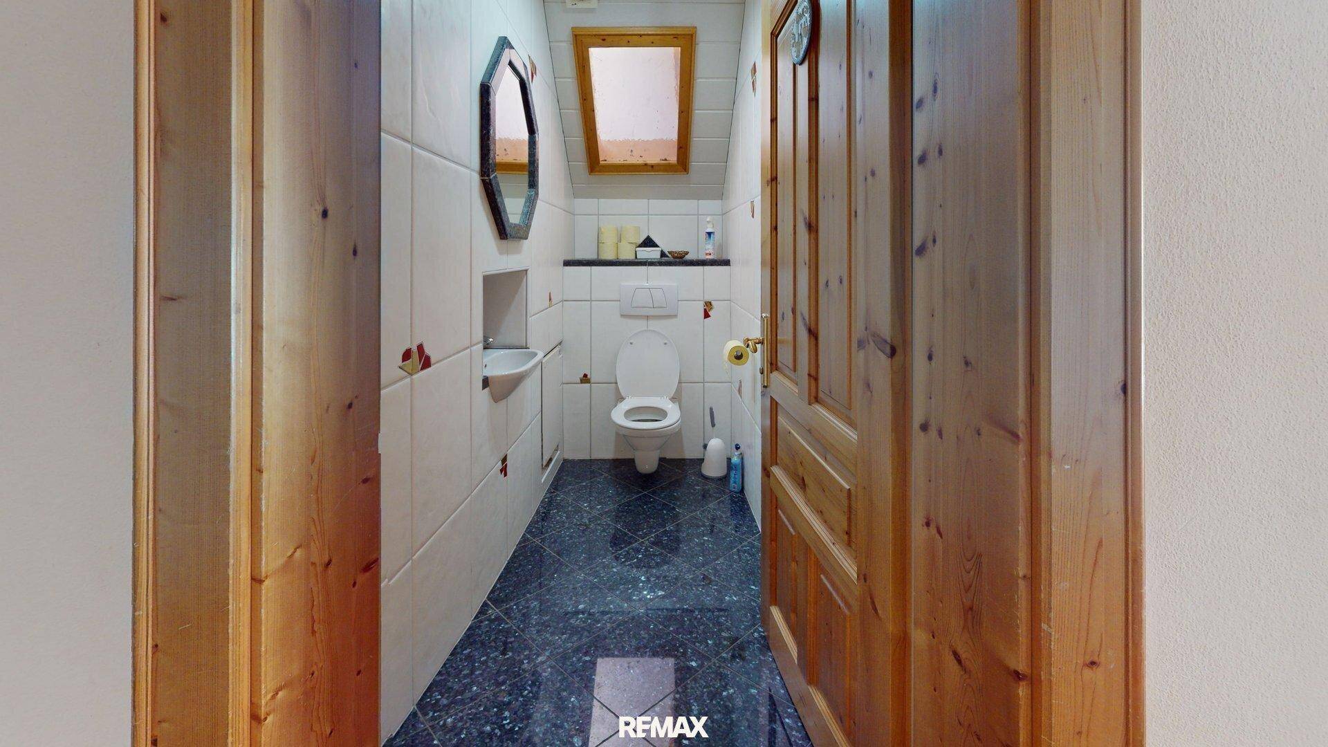 Kleines WC mit dunklen Fliesen, Holzdecke und Dachfenster für natürliches Licht.