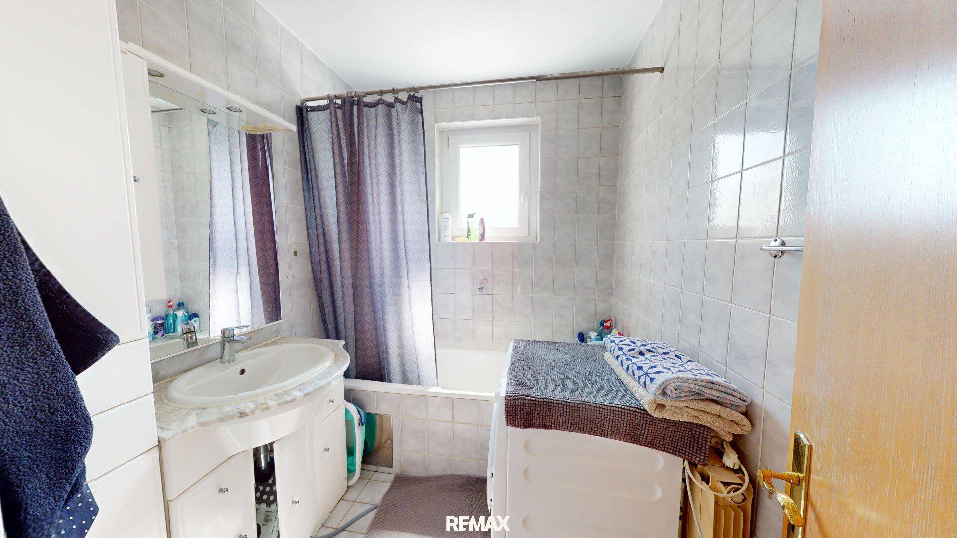 Funktionales Badezimmer mit Badewanne, Waschbecken, Waschmaschine und einem Fenster.