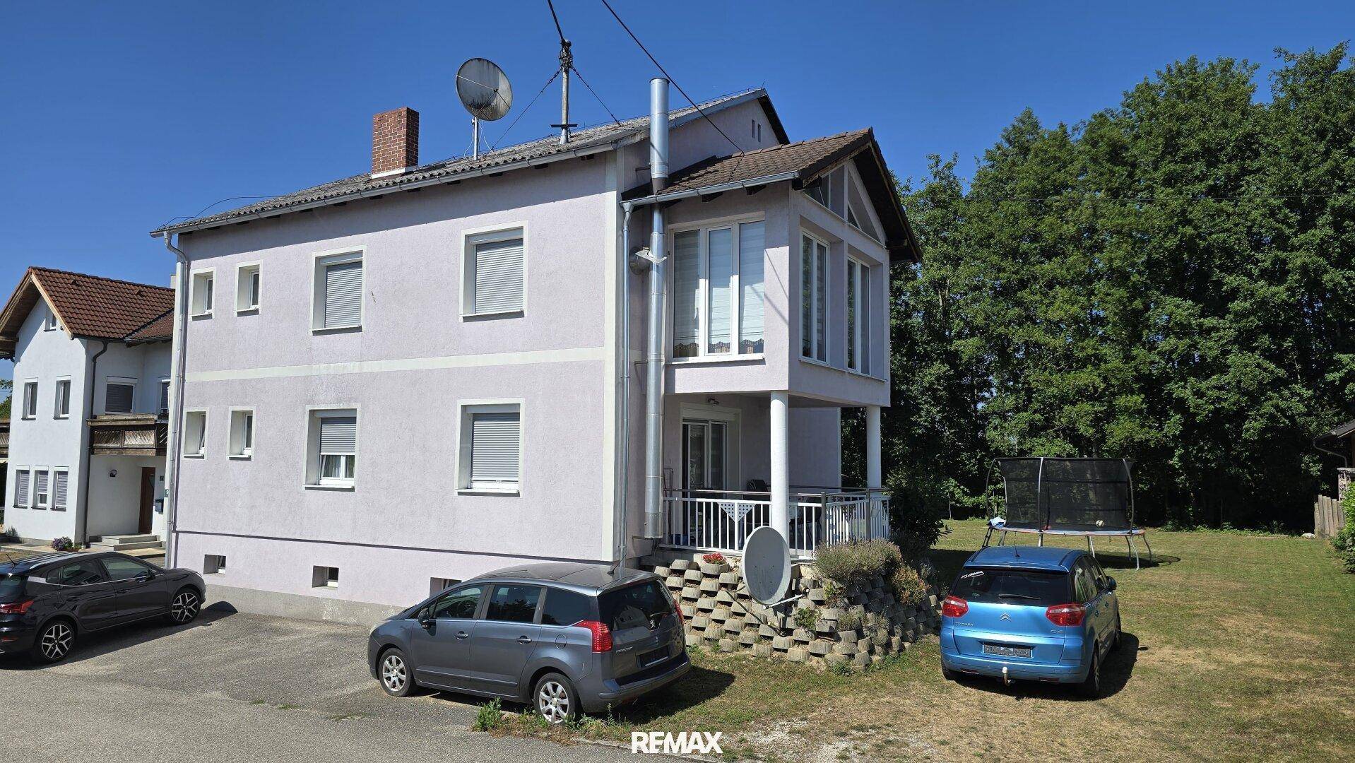 Freistehendes Haus mit heller Fassade, Wintergarten und großem Gartenbereich mit Trampolin.