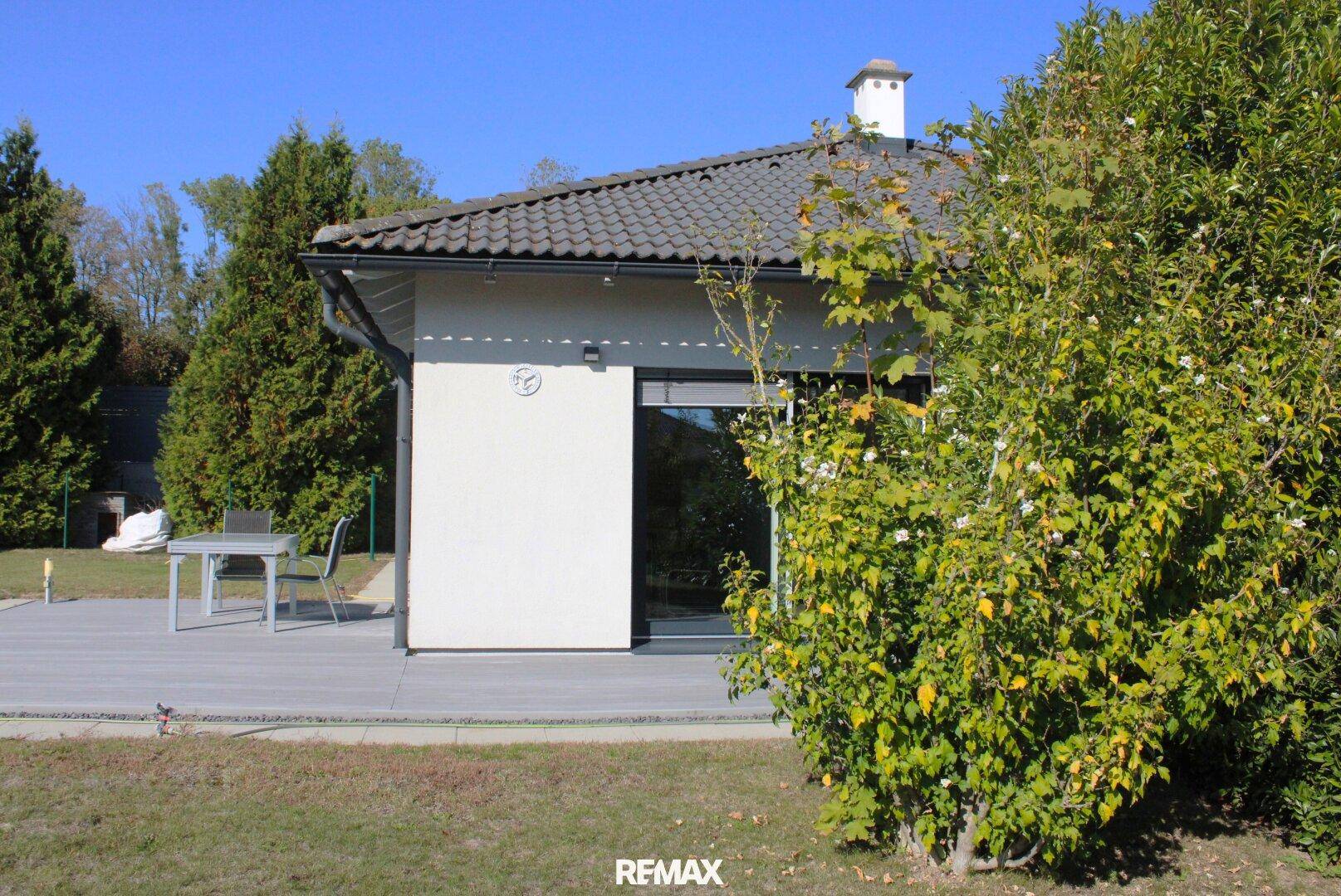 Ansicht des modernen Einfamilienhauses mit Garten und Terrasse unter blauem Himmel.