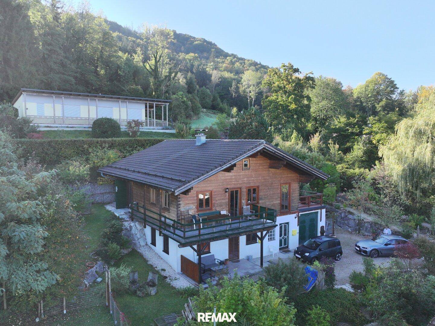 Charmantes Holzchalet mit Balkon, umgeben von üppiger Natur und bewaldeten Hügeln.
