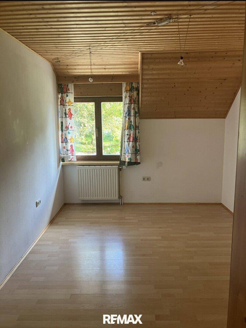 Helles Zimmer mit Laminatboden, Holzdecke und Fenster mit Blick ins Grüne.