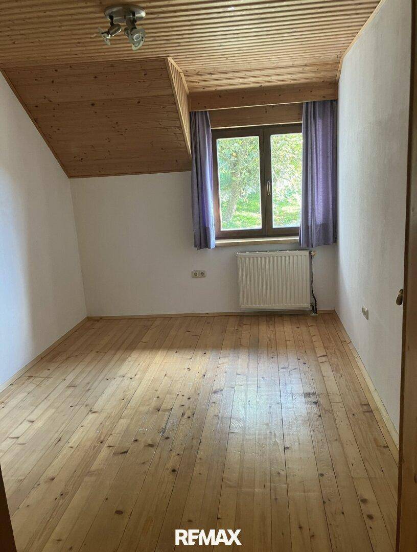 Geräumiges Zimmer mit Holzplankenboden, Holzdecke und Fenster mit Blick ins Grüne.