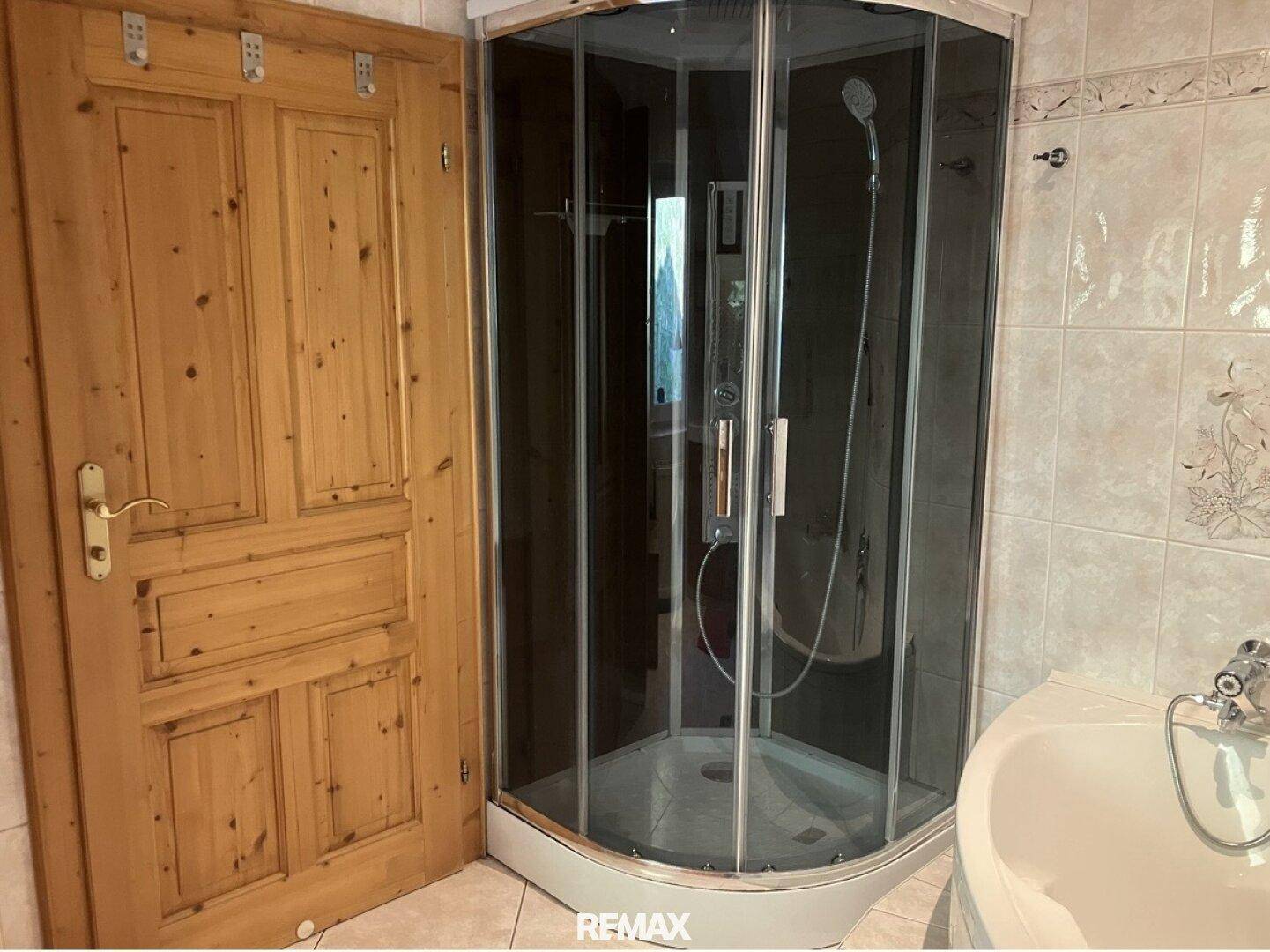 Badezimmer mit Duschkabine und Holztür, gefliest in hellen Tönen.