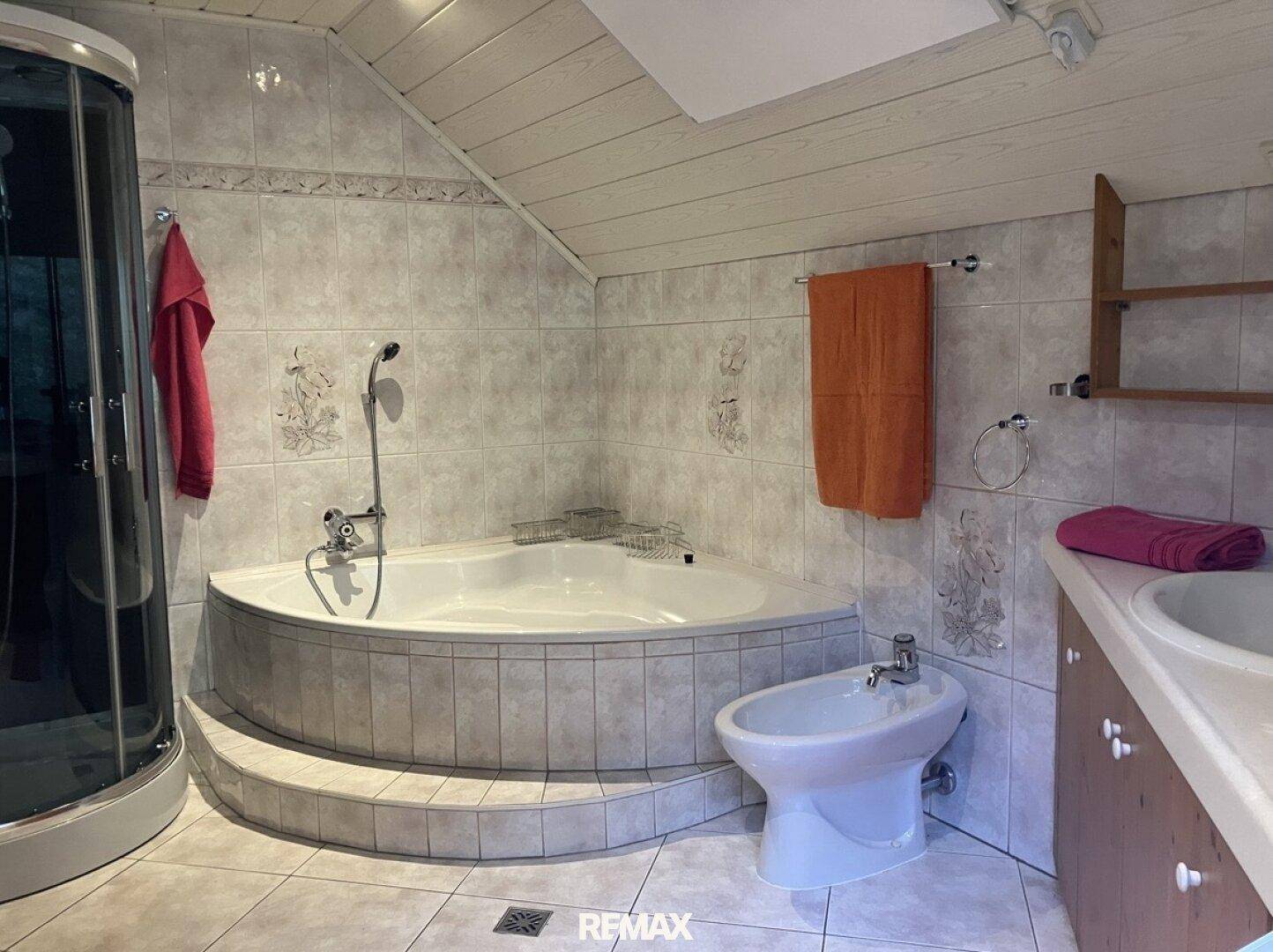 Geräumiges Badezimmer mit Eckbadewanne, Bidet und Duschkabine unter Dachschräge.