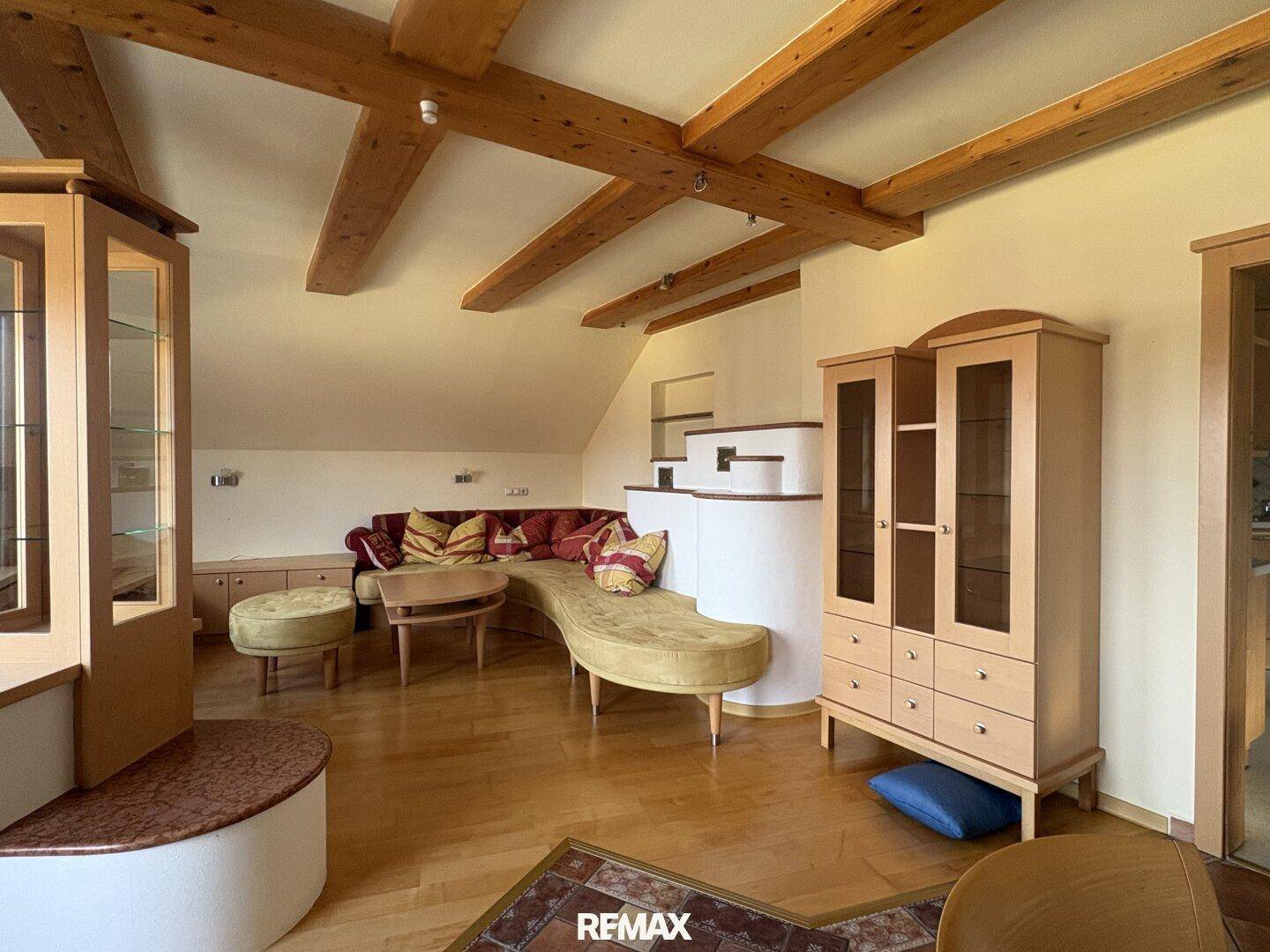 Geräumiges Wohnzimmer mit Holzbalken, Parkettboden und gemütlicher Sitzecke unter Dachschrägen.