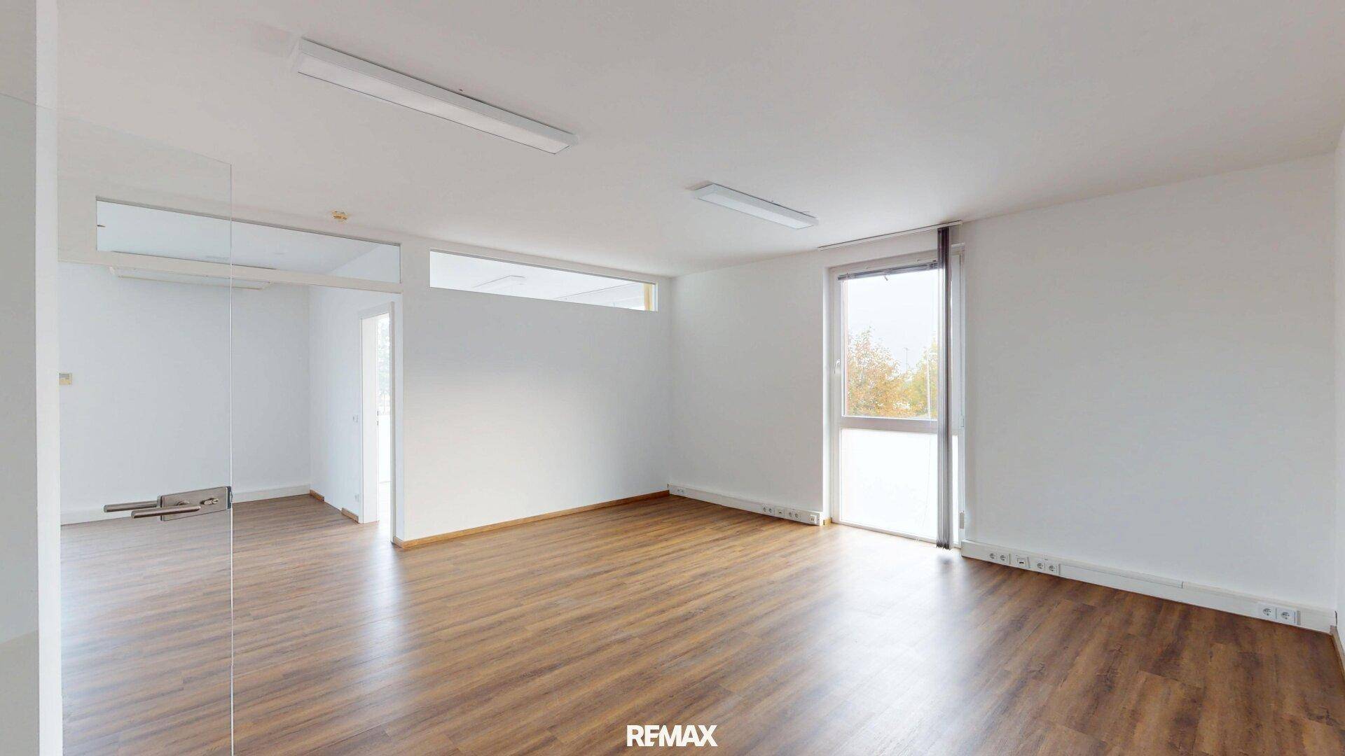Heller Büroraum mit Holzoptikboden und breiten Fenstern, ideal für flexible Arbeitsplatzgestaltung.