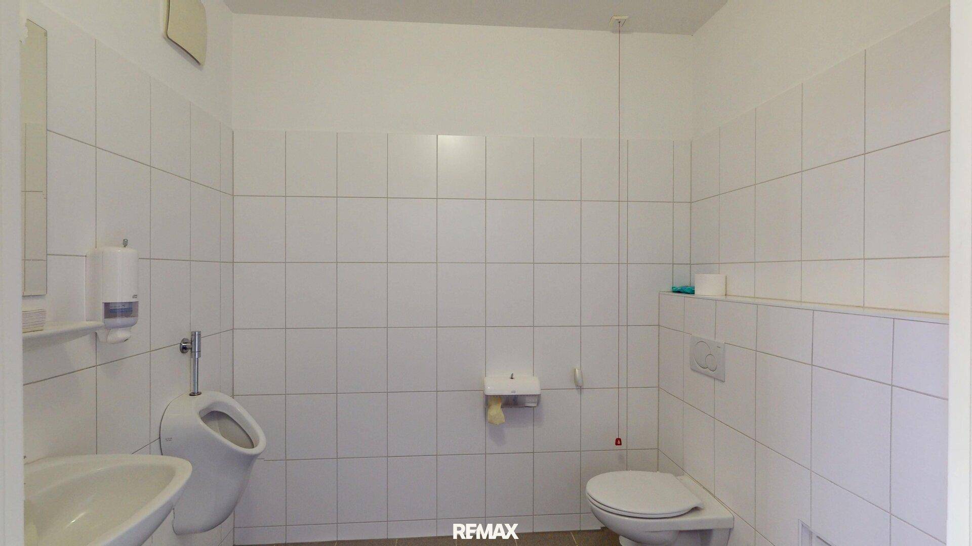 Gefliestes WC mit Urinal und Waschbecken, in sauberem und funktionalem Zustand.