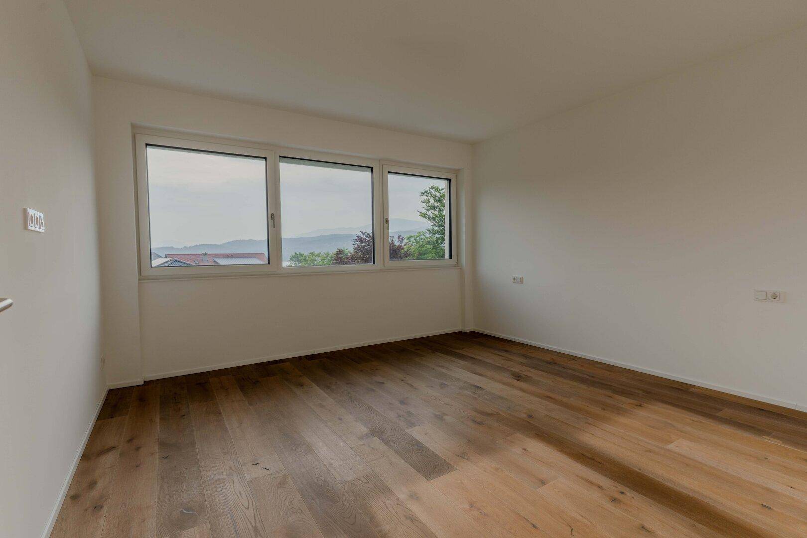 Helles Schlafzimmer mit Holzboden und großen Fenstern, die einen weiten Blick bieten.