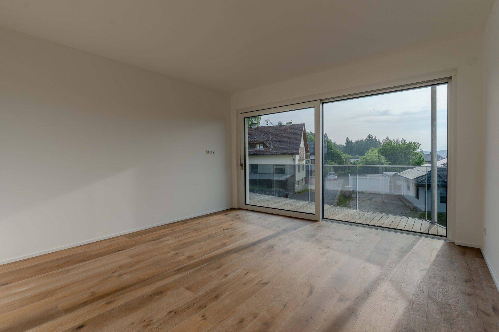 Geräumiges Zimmer mit Holzboden und großer Glasschiebetür, die Zugang zum Außenbereich bietet.