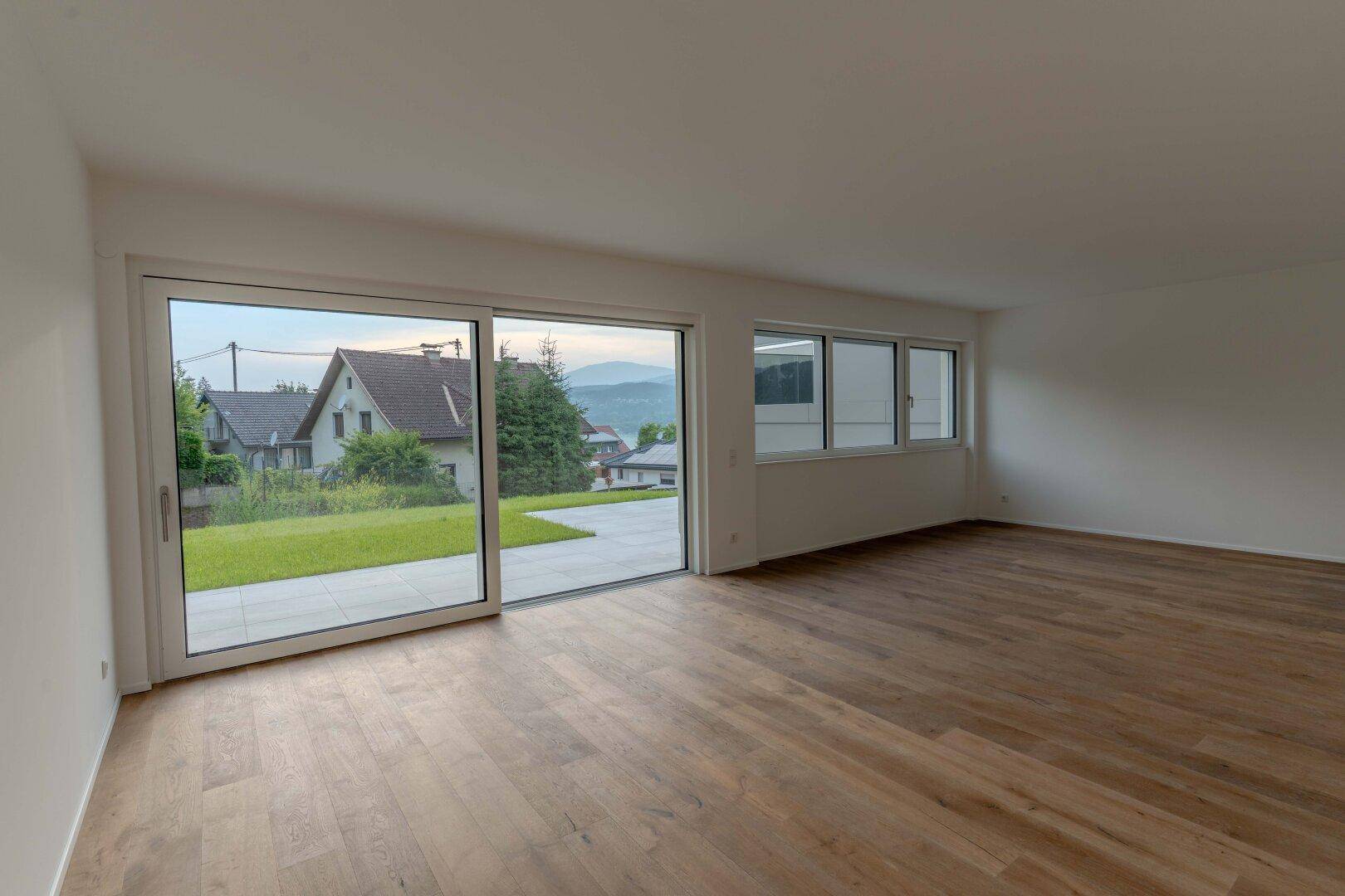 Heller, leerer Wohnraum mit Holzboden, großen Schiebetüren und Blick ins Grüne.