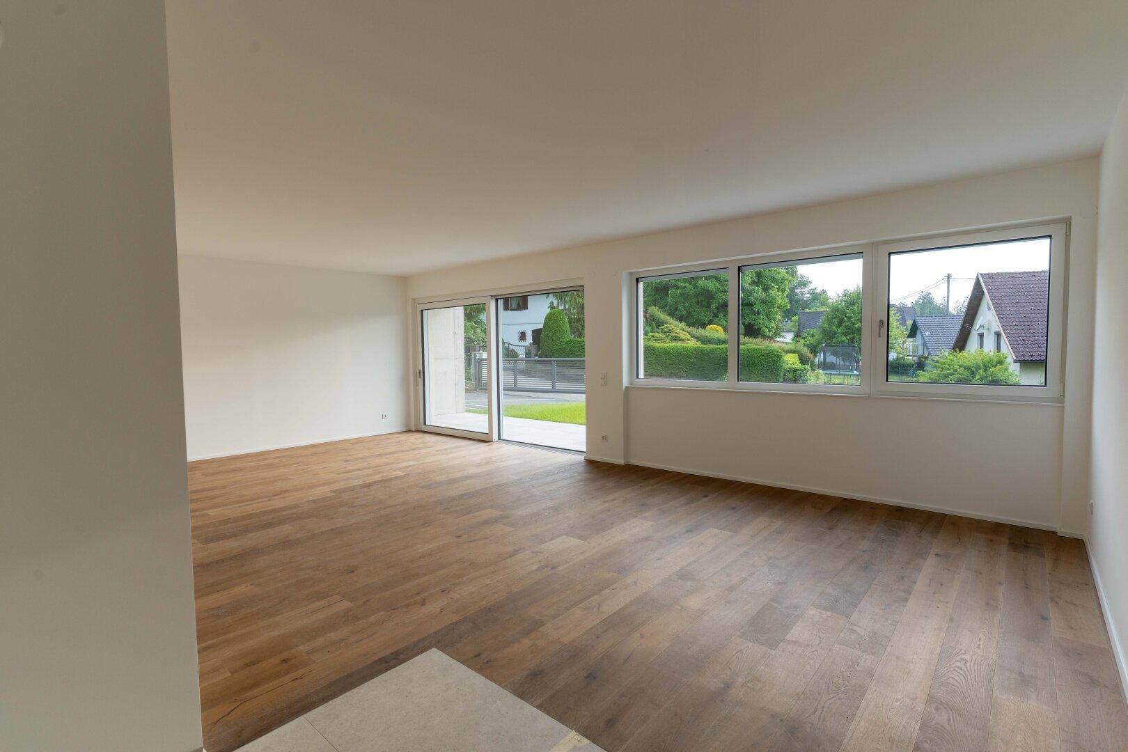 Geräumiger, unmöblierter Wohnbereich mit Holzboden und großen Fenstern zur Gartenseite.