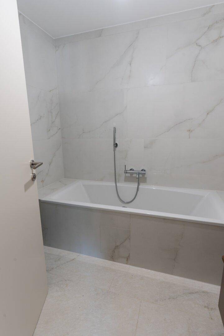 Modernes Badezimmer mit eingebauter Badewanne und eleganten Marmor-Effekt-Fliesen.