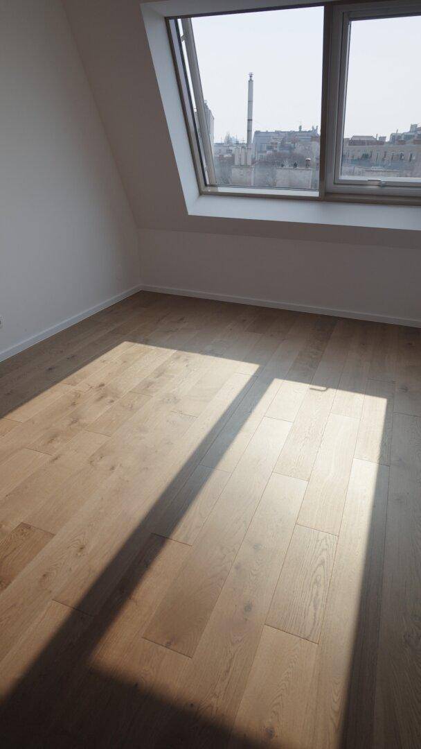 Leerer Raum im Dachgeschoss mit Holzboden, schrägen Wänden und viel Tageslicht durch Dachfenster.
