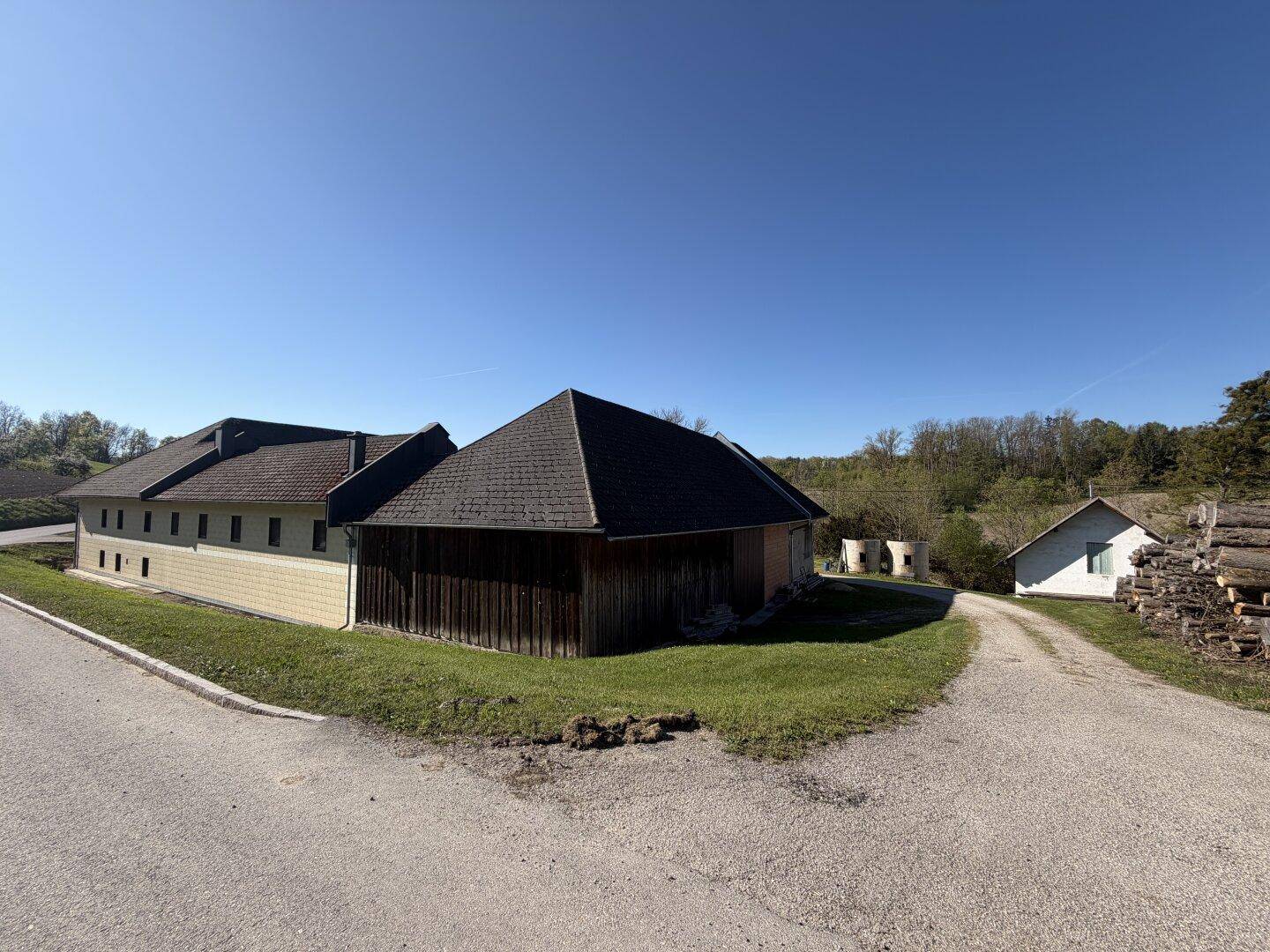 Ländliches Anwesen mit Holzscheune und weiten Feldern unter klarem blauem Himmel.