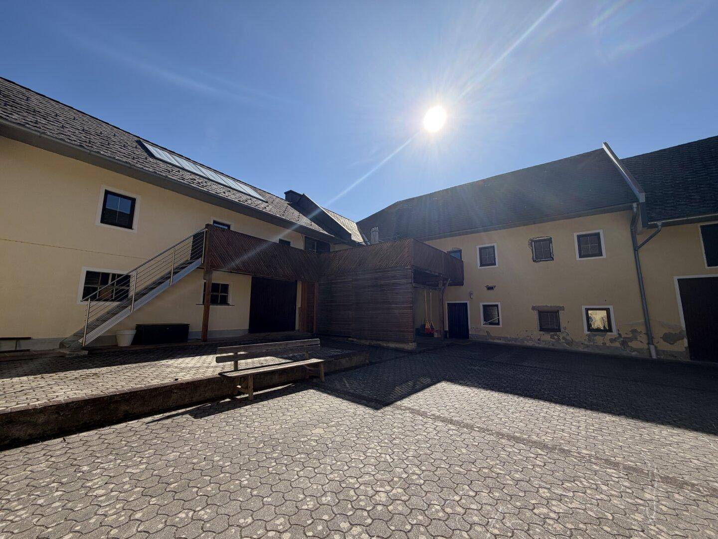 Sonniger Innenhof mit Steinpflaster, externer Treppe und Gebäudefassaden.