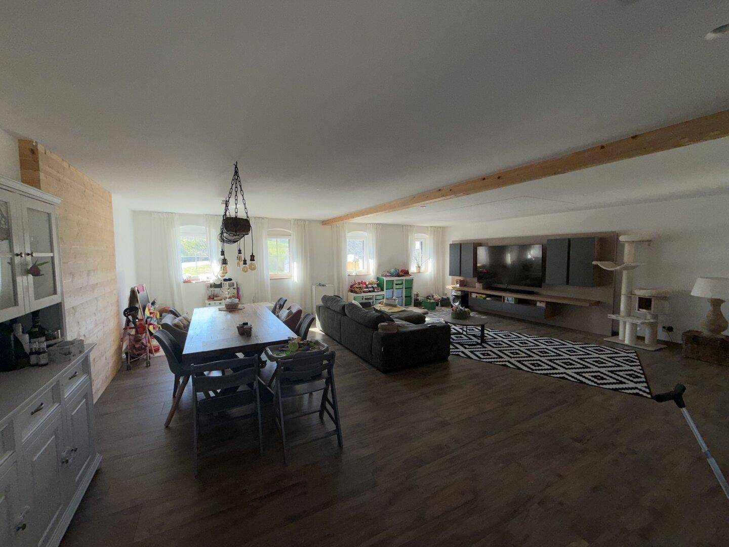 Geräumiger offener Wohn- und Essbereich mit Holzboden, großem Esstisch und TV-Wand.
