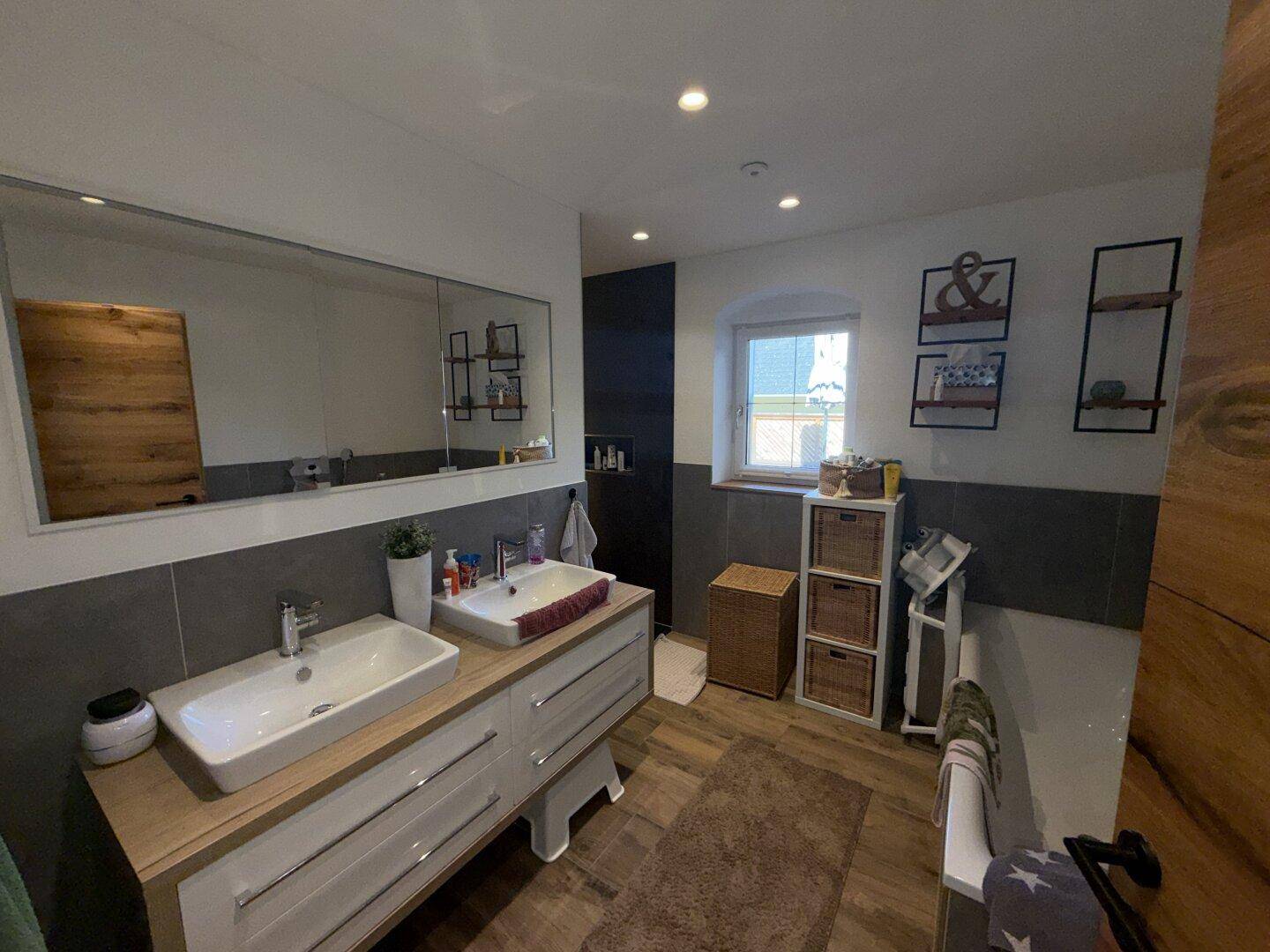 Modernes Badezimmer mit Doppelwaschbecken, großem Spiegel und Fenster für Tageslicht.