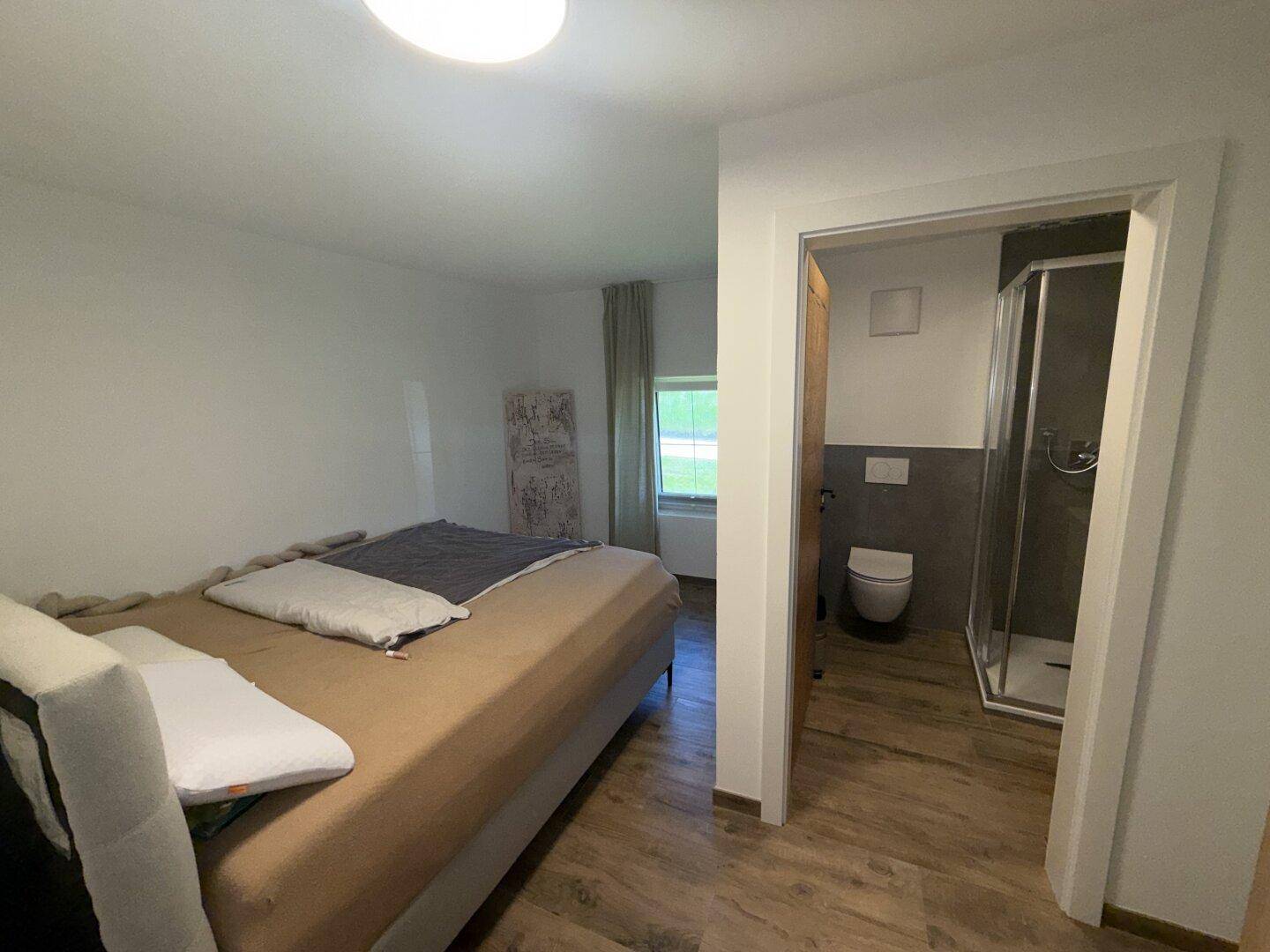 Schlafzimmer mit Bett und direktem Zugang zu einem modernen Duschbad.