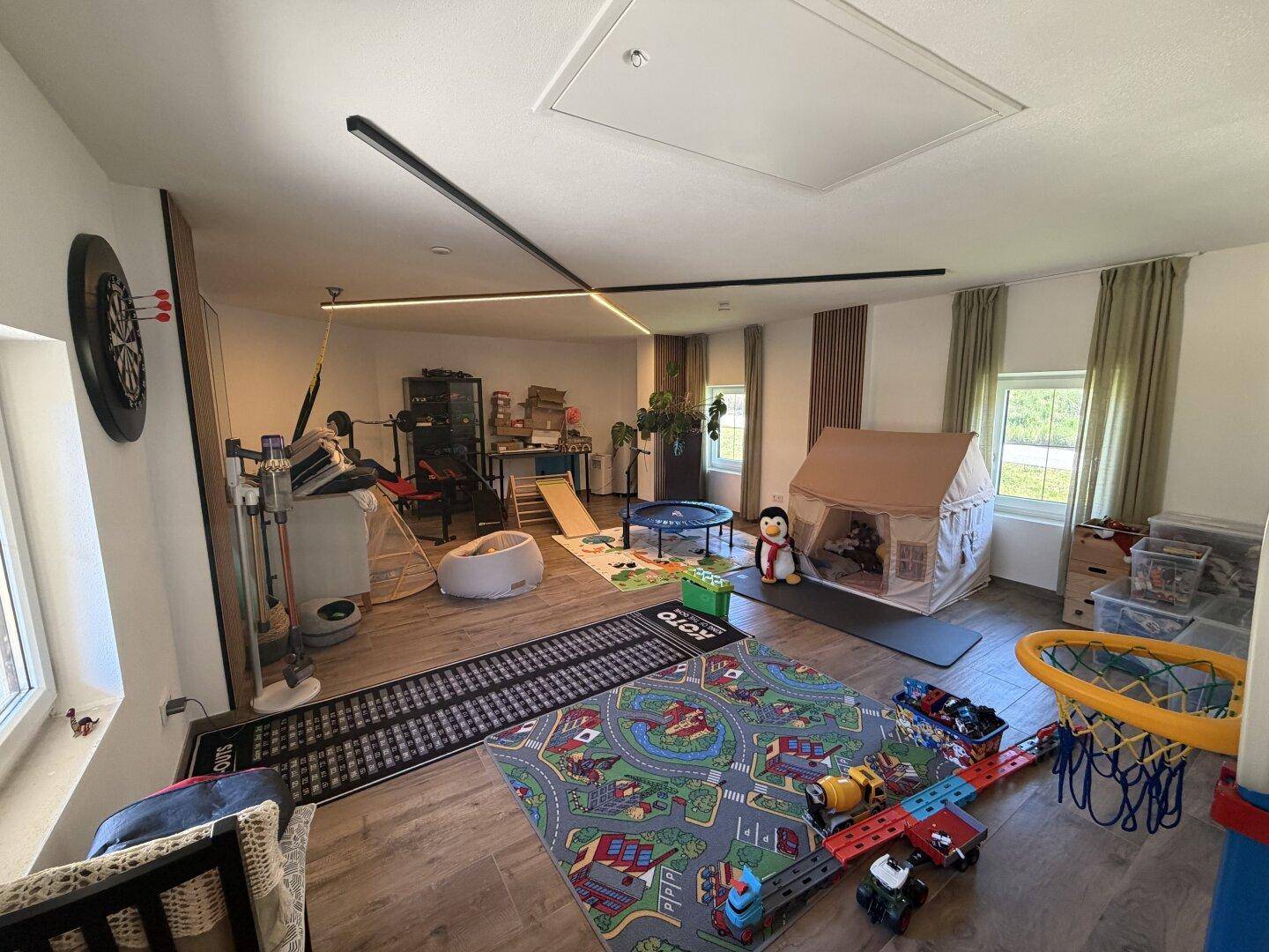 Großer Mehrzweckraum, eingerichtet als Spielbereich und Fitnessraum mit Holzboden.