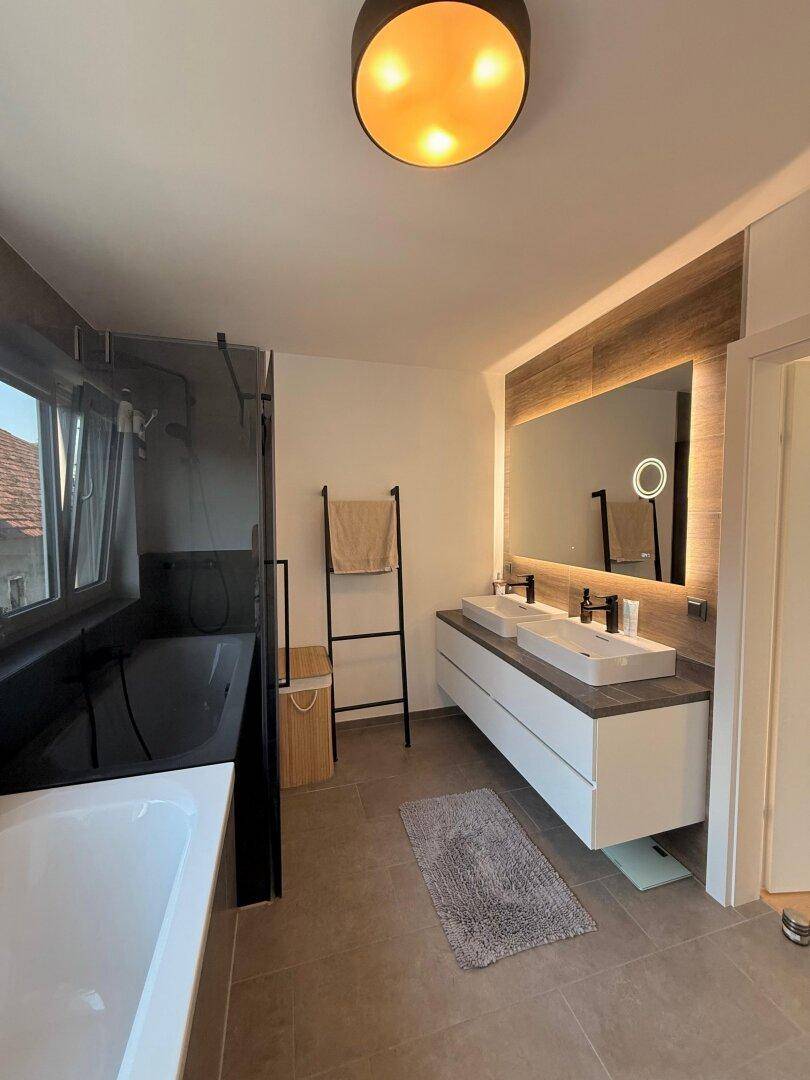 Elegantes Badezimmer mit Doppelwaschbecken, großem beleuchteten Spiegel und begehbarer Dusche.