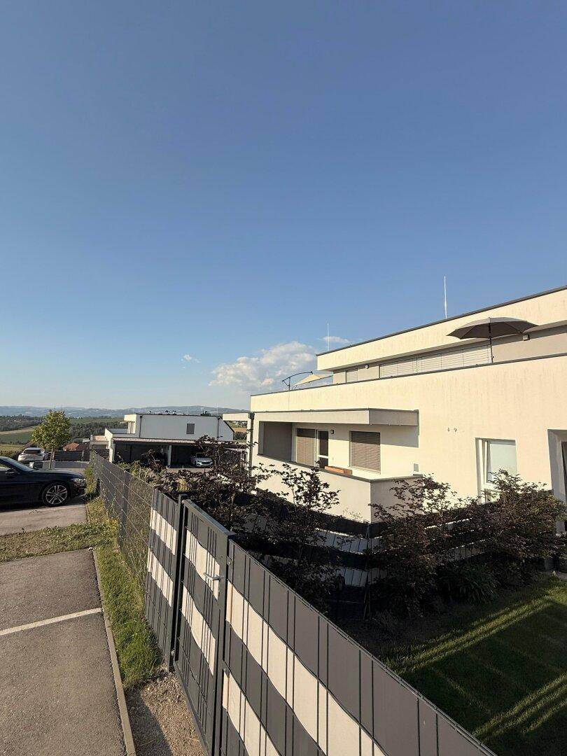 Moderne Architektur des Gebäudes mit Flachdach, umgeben von grüner Landschaft und Zaun.