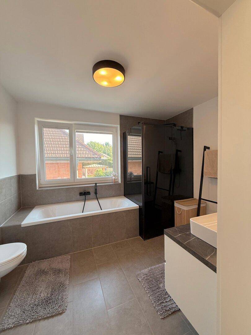 Modernes Badezimmer mit Badewanne, begehbarer Dusche, WC und Fenster für Tageslicht.