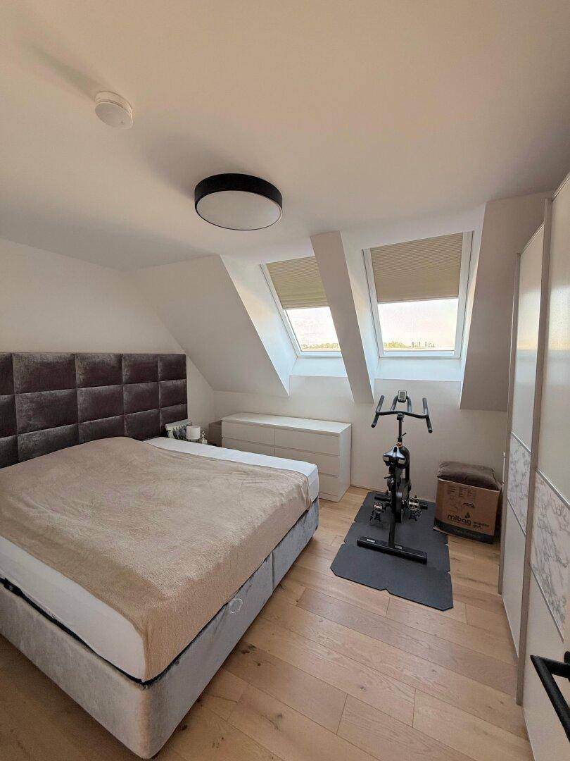 Gemütliches Schlafzimmer mit großem Bett, Trainingsgerät und zwei Dachfenstern für Helligkeit.