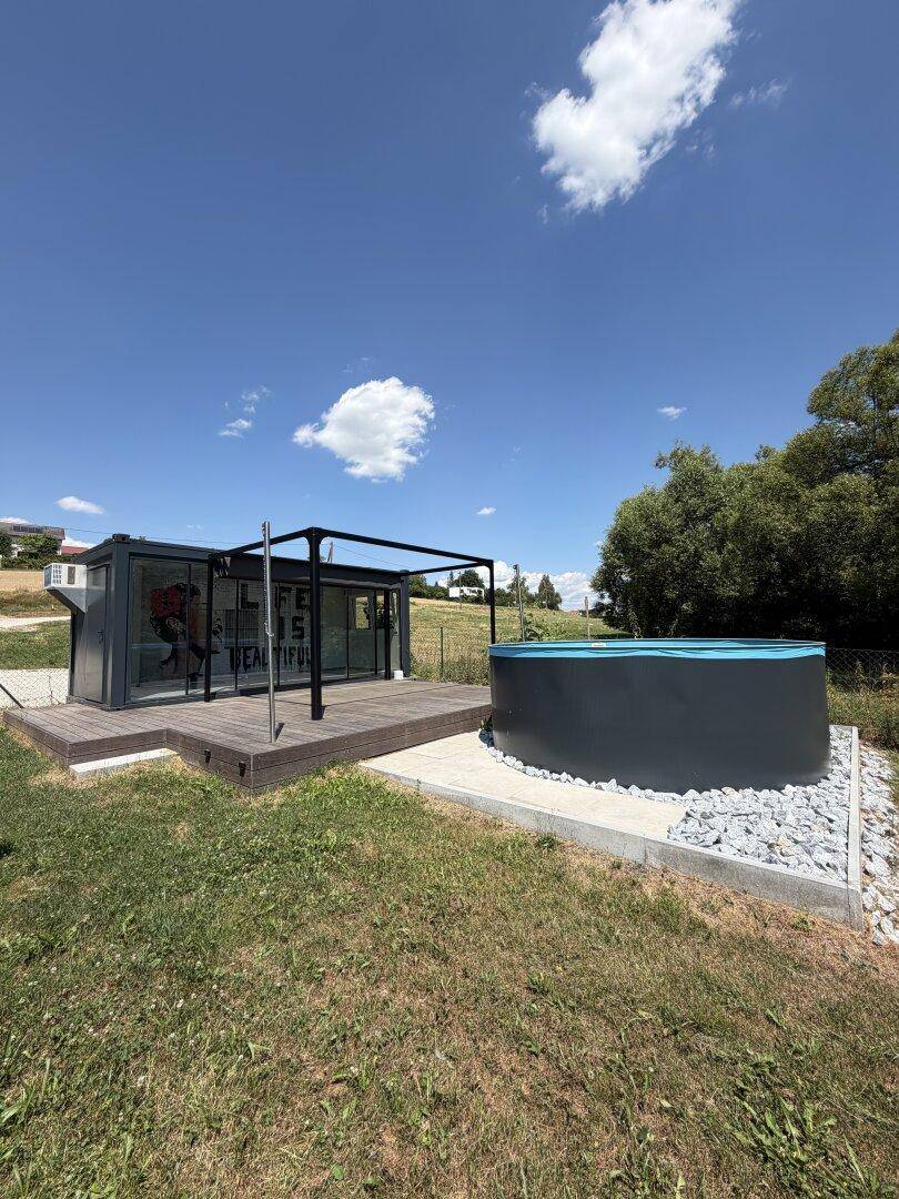 Moderner Anbau mit Glasfront und Holzterrasse neben dem Pool im Grünen.