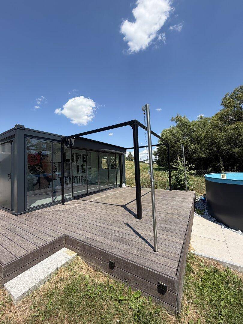 Holzterrasse mit moderner Überdachung und Blick auf den Pool und die Natur.