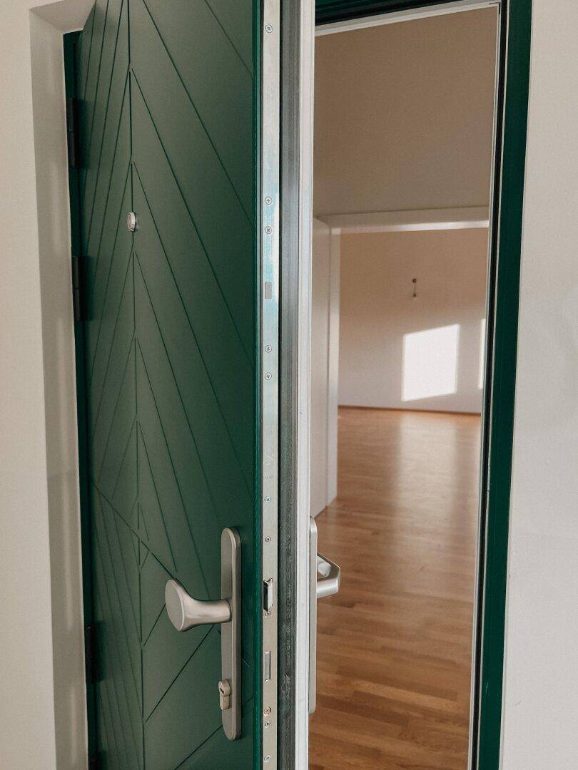 Grüne Eingangstür mit modernem Design und Blick in den hellen Innenbereich.