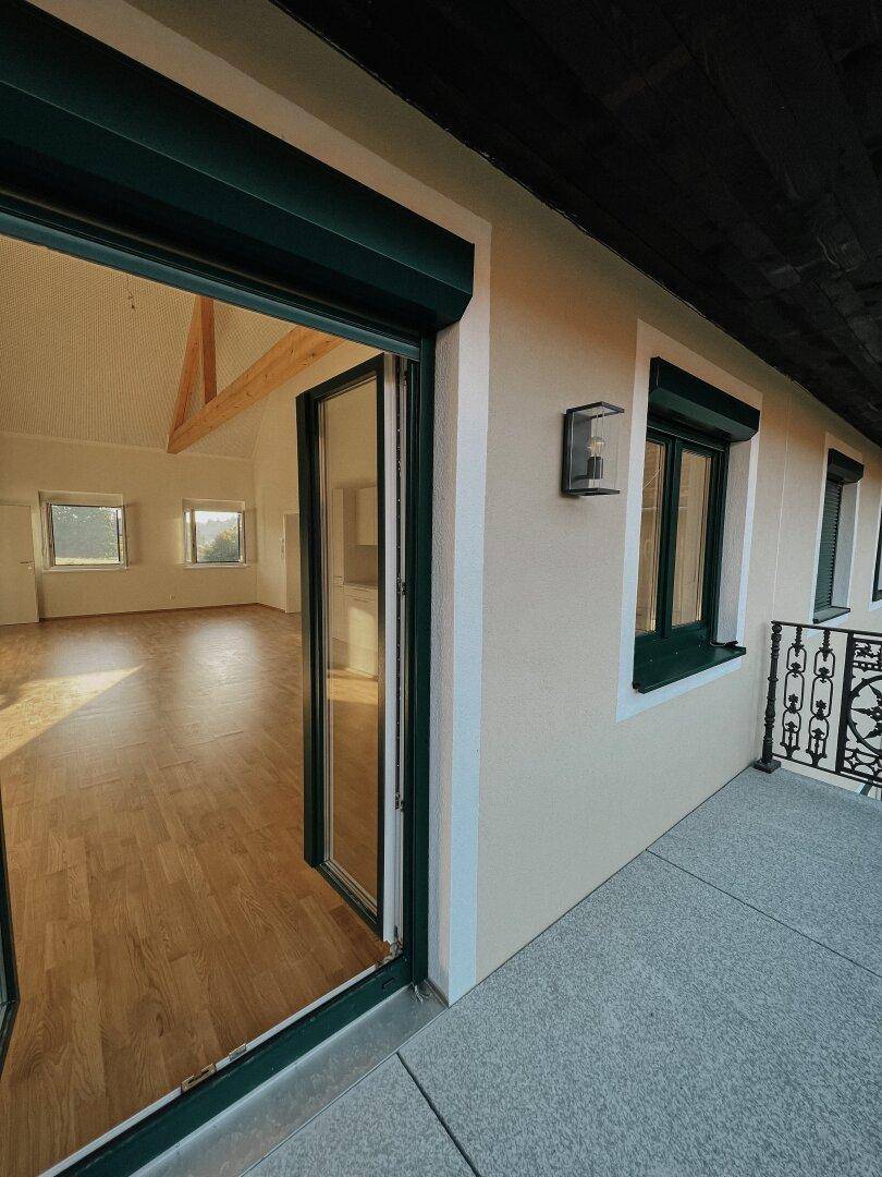 Balkon mit Zugang zum hellen Innenbereich und Blick auf die ländliche Umgebung.