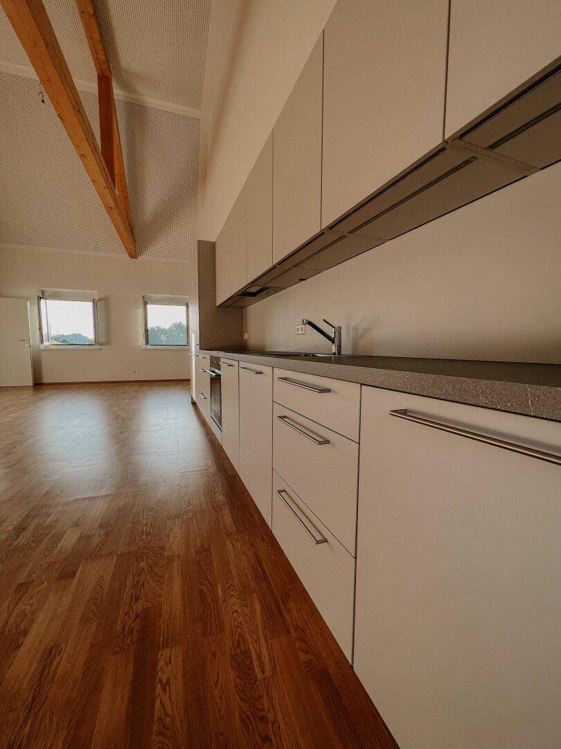 Moderne Einbauküche mit weißen Schränken, dunkler Arbeitsplatte und integriertem Backofen.