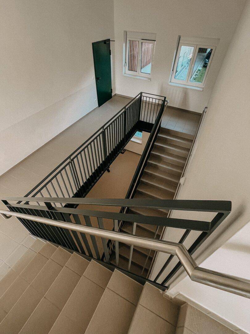 Helles Treppenhaus mit Metallgeländer und Fenstern, die Tageslicht hereinlassen.