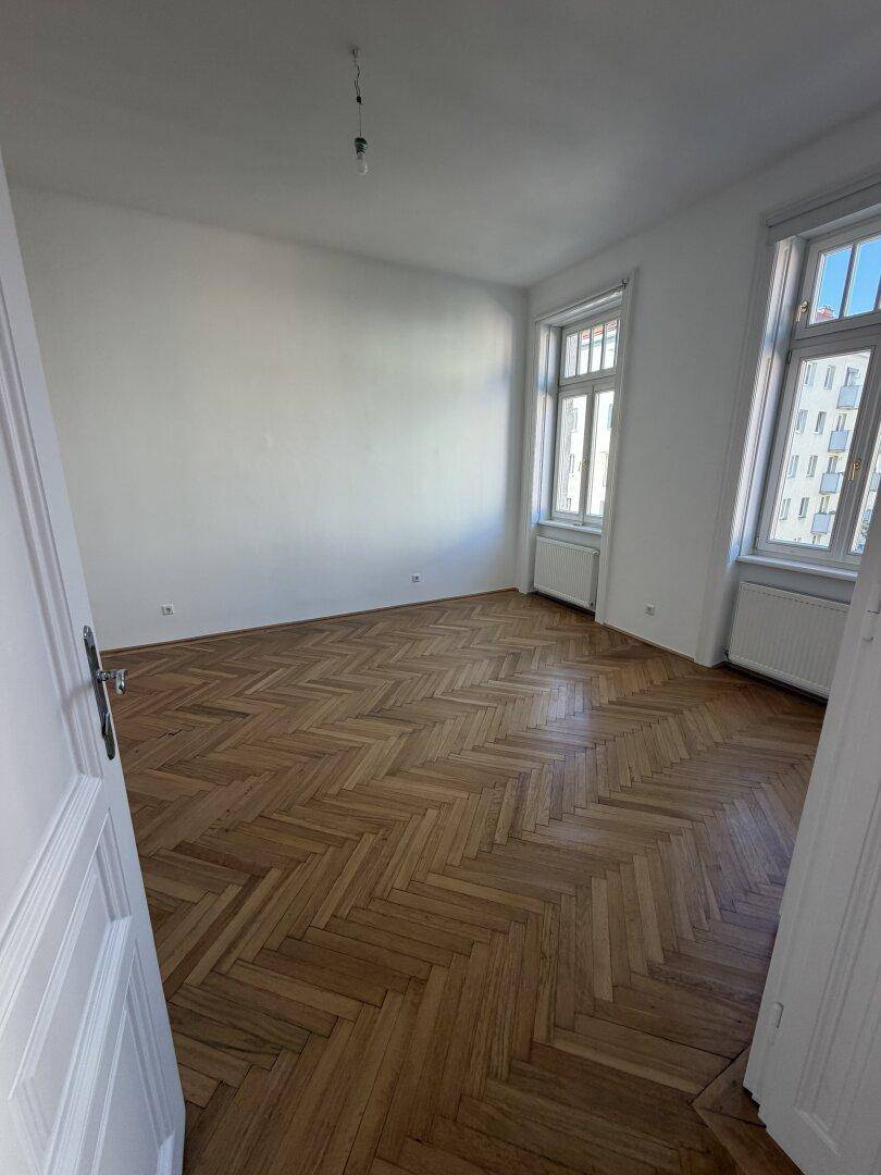 Helles, unmöbliertes Zimmer mit Fischgrätparkett und zwei Fenstern, bereit zur individuellen Einrichtung.