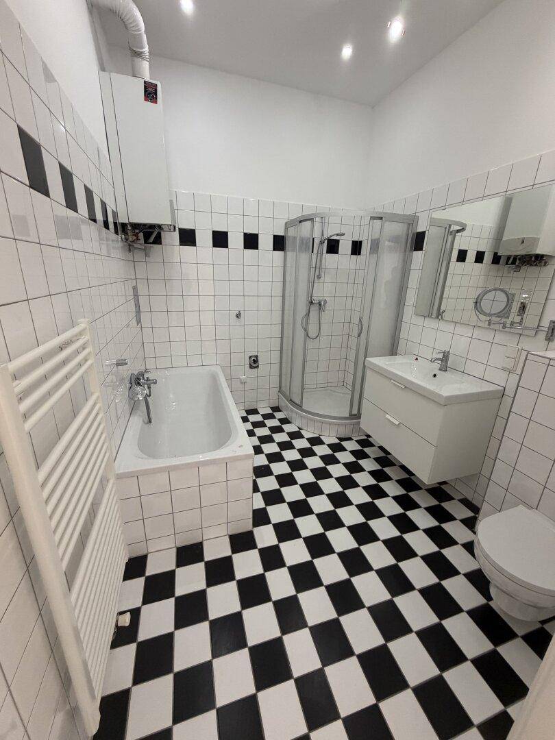 Modernes Badezimmer mit Badewanne, Dusche und schwarz-weißem Schachbrettmuster-Fliesenboden.