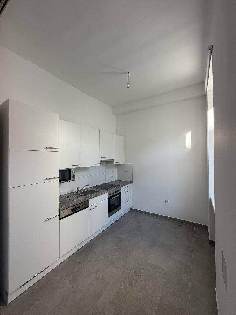 Moderne Einbauküche mit weißen Schränken, integrierten Geräten und grauen Fliesenboden.