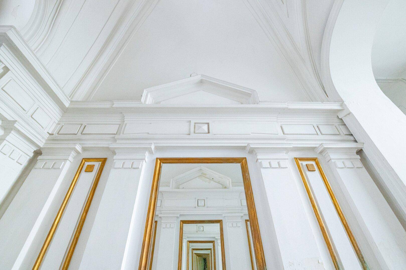 Detailaufnahme einer prunkvollen Decke und Wandverkleidung mit Stuck und goldenen Akzenten.