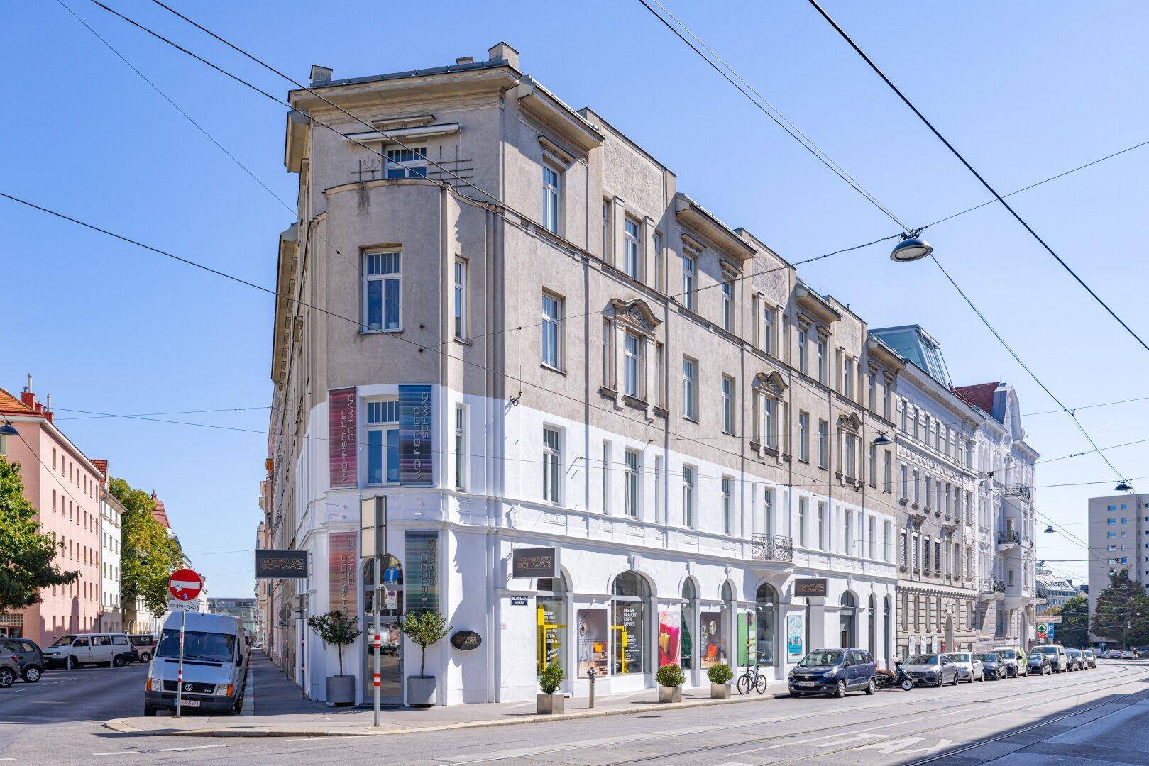 Historisches Eckgebäude mit Geschäften im Erdgeschoss und Wohnungen darüber in urbaner Umgebung.