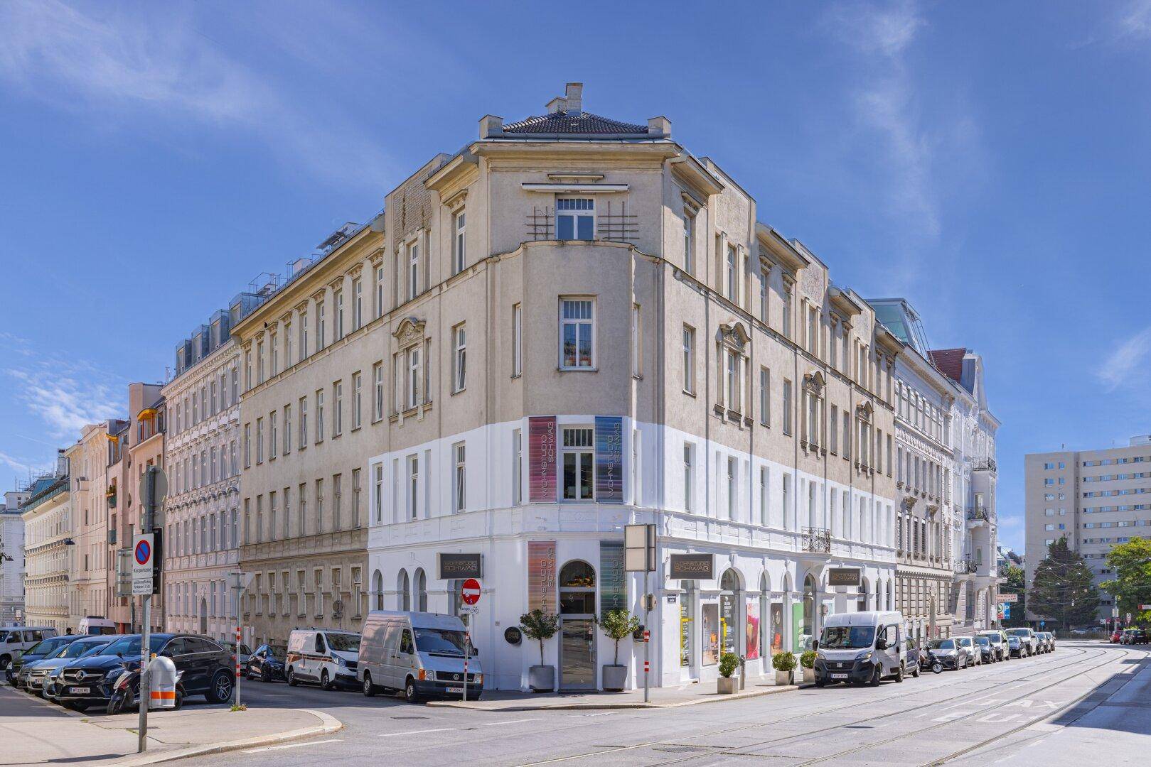 Historisches Eckgebäude mit Geschäften im Erdgeschoss und Wohnungen darüber in urbaner Umgebung.