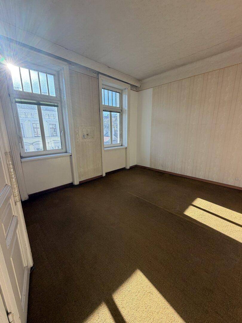 Helles Zimmer mit Teppichboden und mehreren Fenstern, die viel Sonnenlicht hereinlassen.