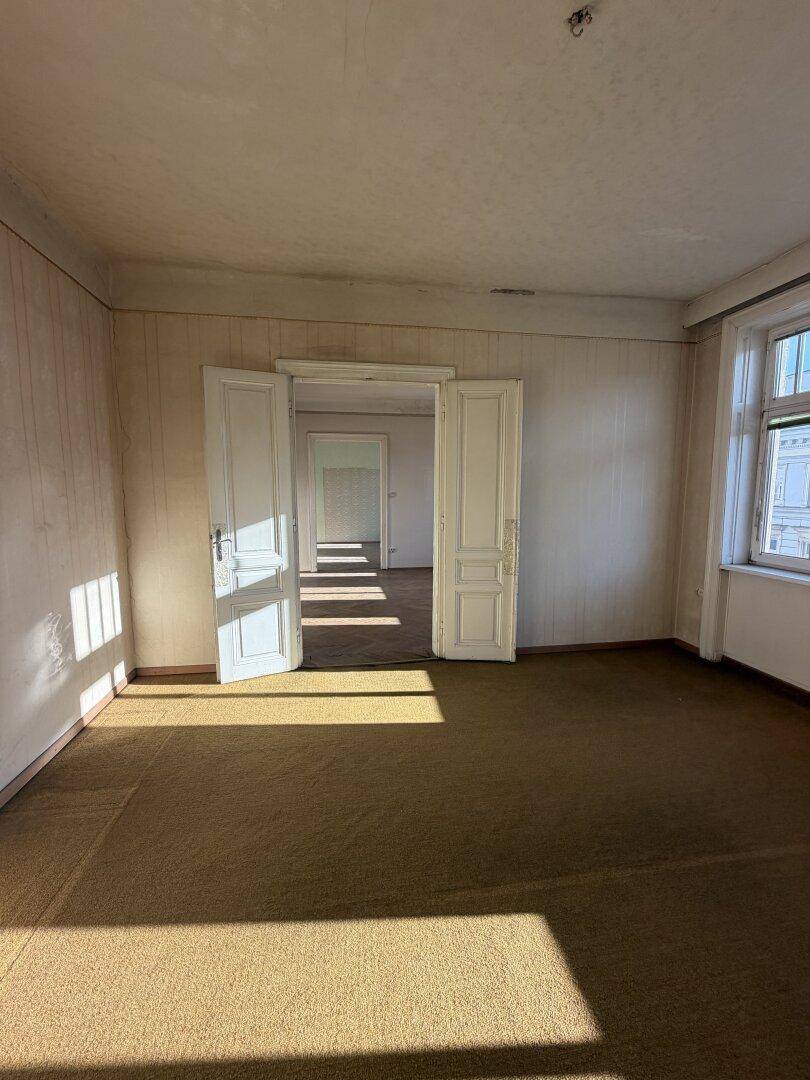 Geräumiges Zimmer mit Teppichboden und doppelten Flügeltüren, die zu einem weiteren Raum führen.