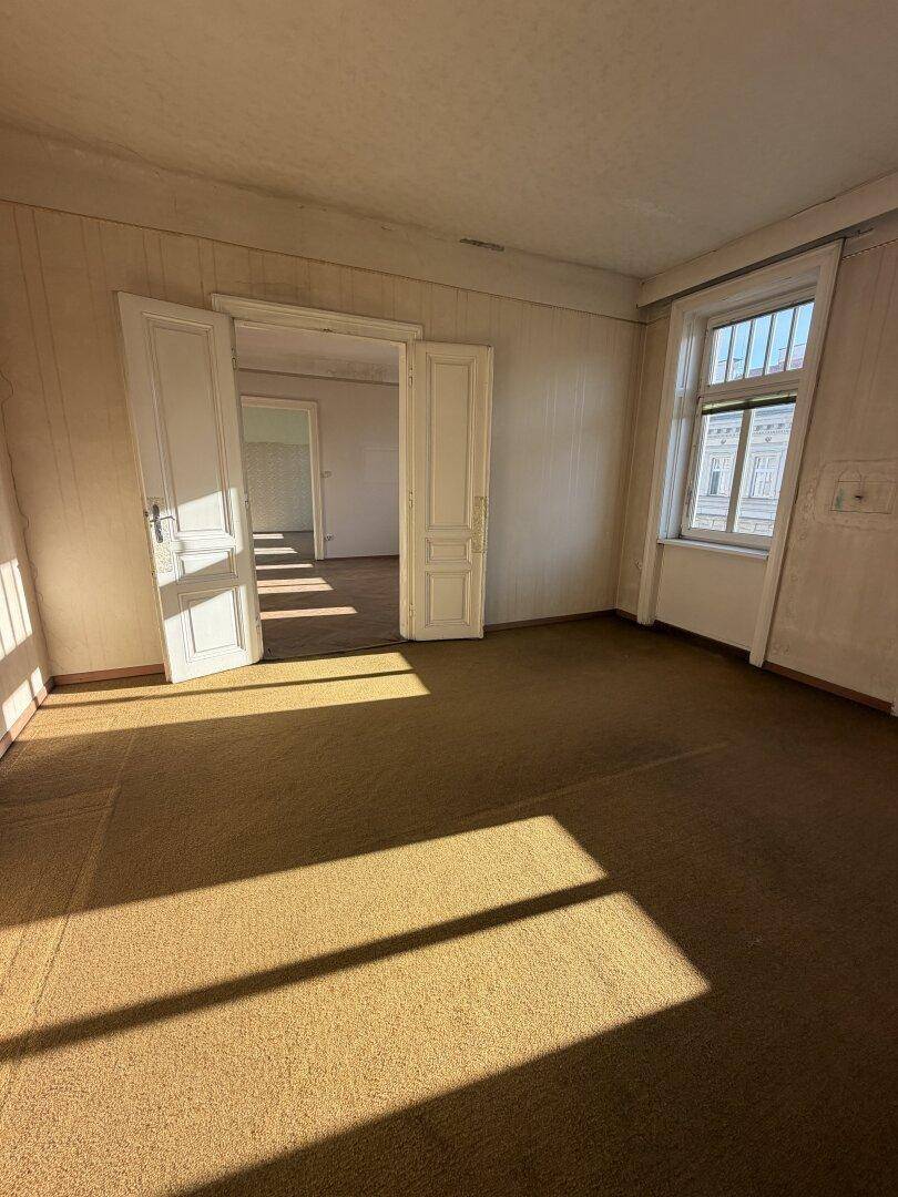 Geräumiges Zimmer mit Teppichboden und doppelten Flügeltüren, die zu einem weiteren Raum führen.